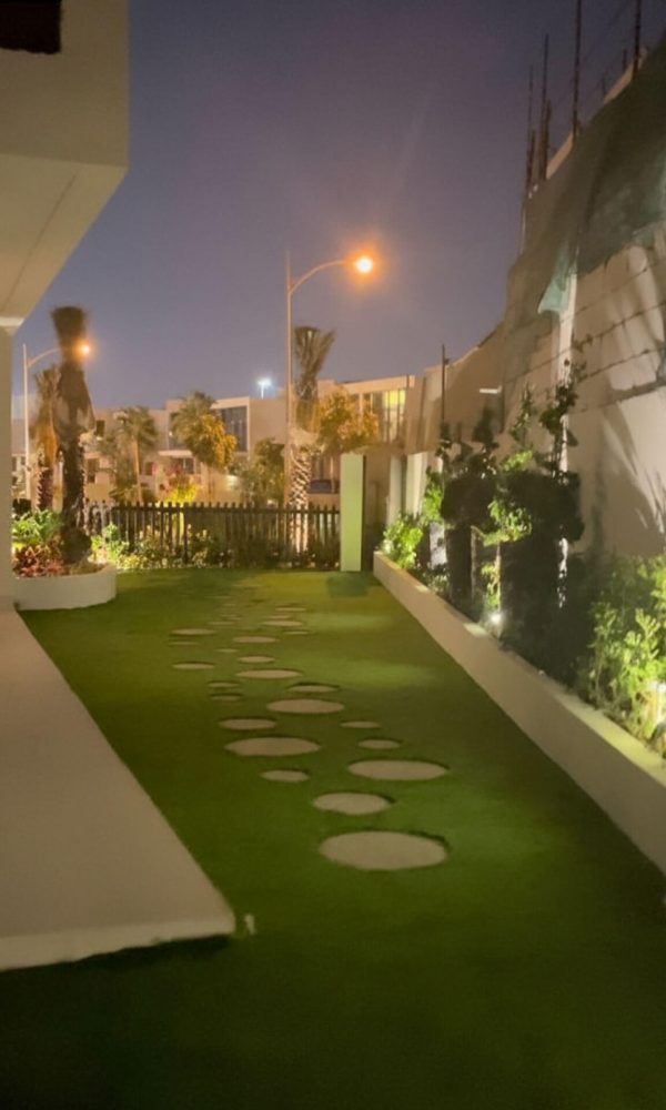 Modern garden pathway with stepping stones, lush green artificial turf, and elegant outdoor lighting design by Design By Shila
