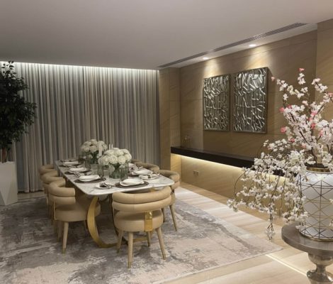 An elegant and modern dining room featuring a long table, upholstered chairs, a tiered chandelier, and a decorative mirror wall